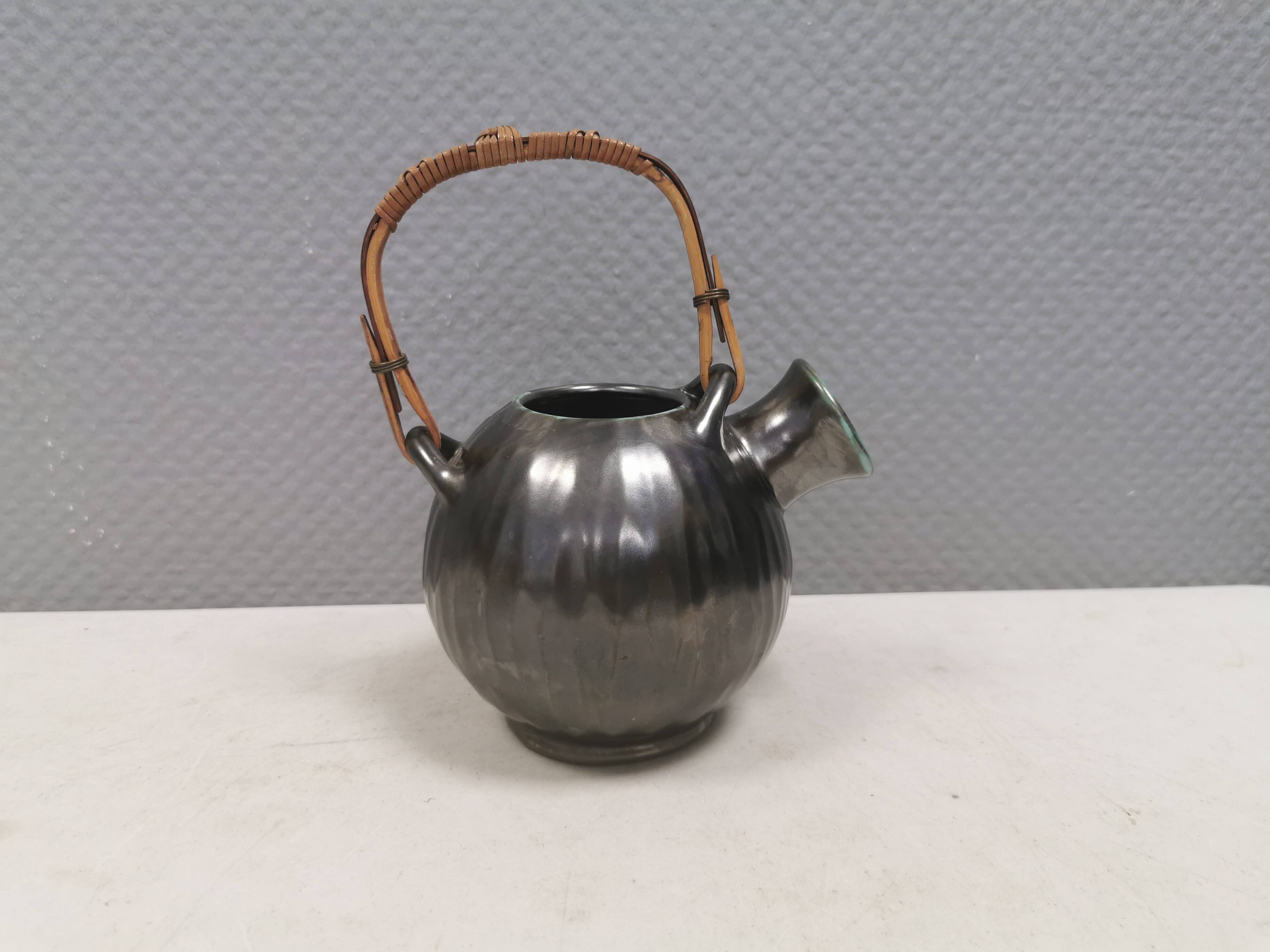 A ceramic jug with a metallic glaze and a handle made of woven raffia.