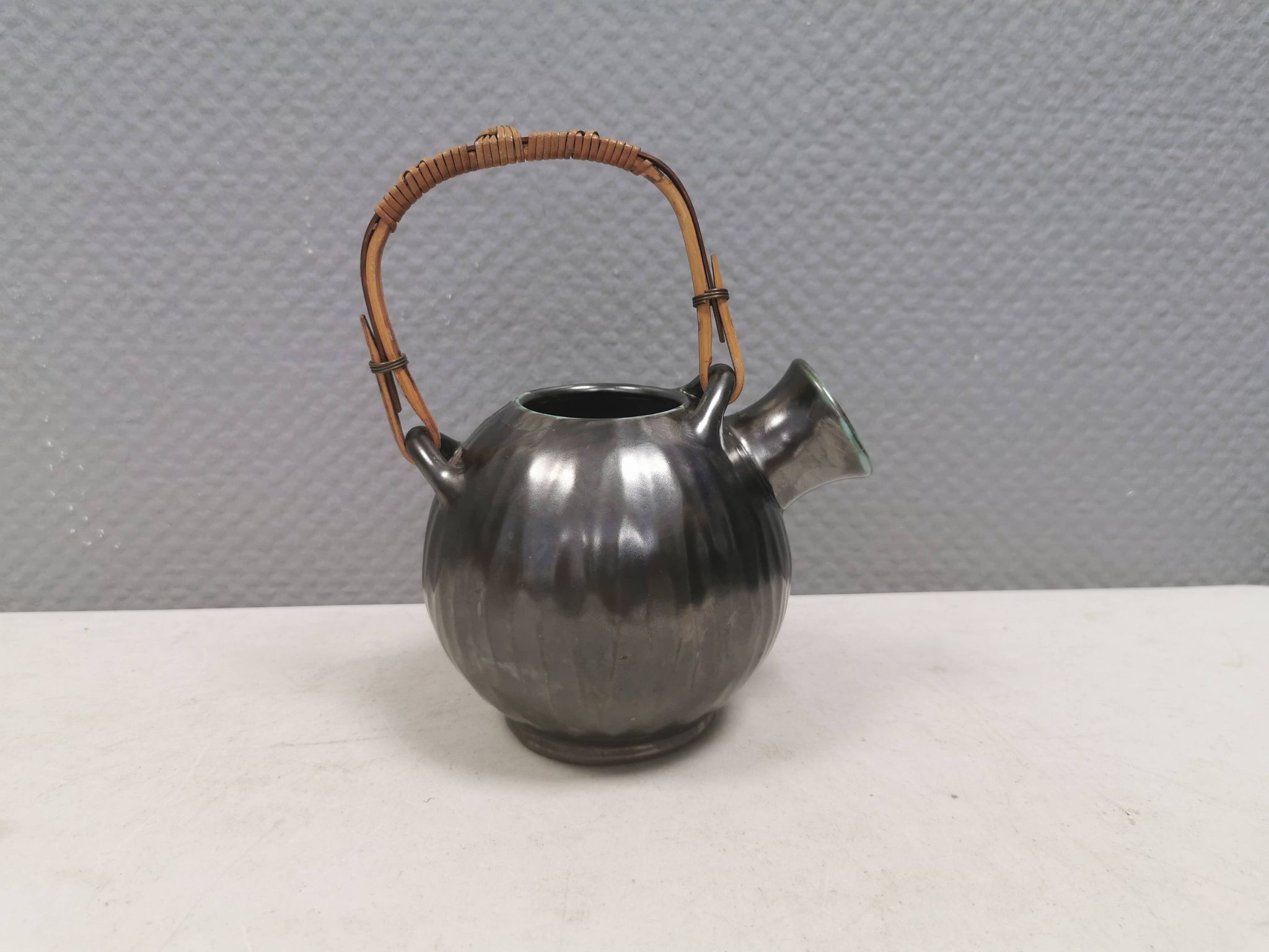 A ceramic jug with a metallic glaze and a handle made of woven raffia.