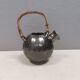 A ceramic jug with a metallic glaze and a handle made of woven raffia.