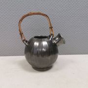 A ceramic jug with a metallic glaze and a handle made of woven raffia.