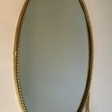 Oval brass mirror surrounded by a cord and adorned