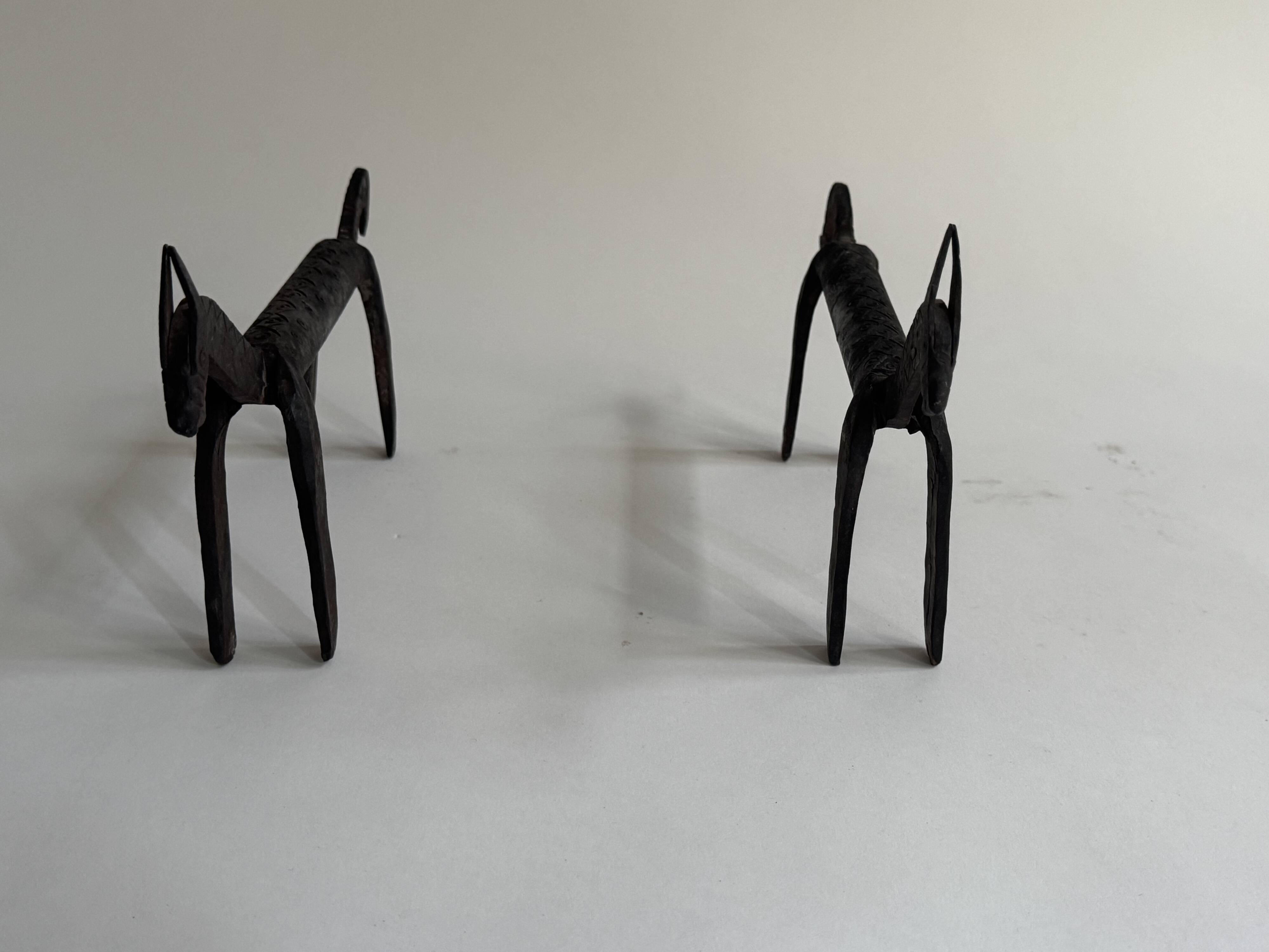 Pair of animal-shaped wrought iron and hammered fire dogs in primitive brutalist style.