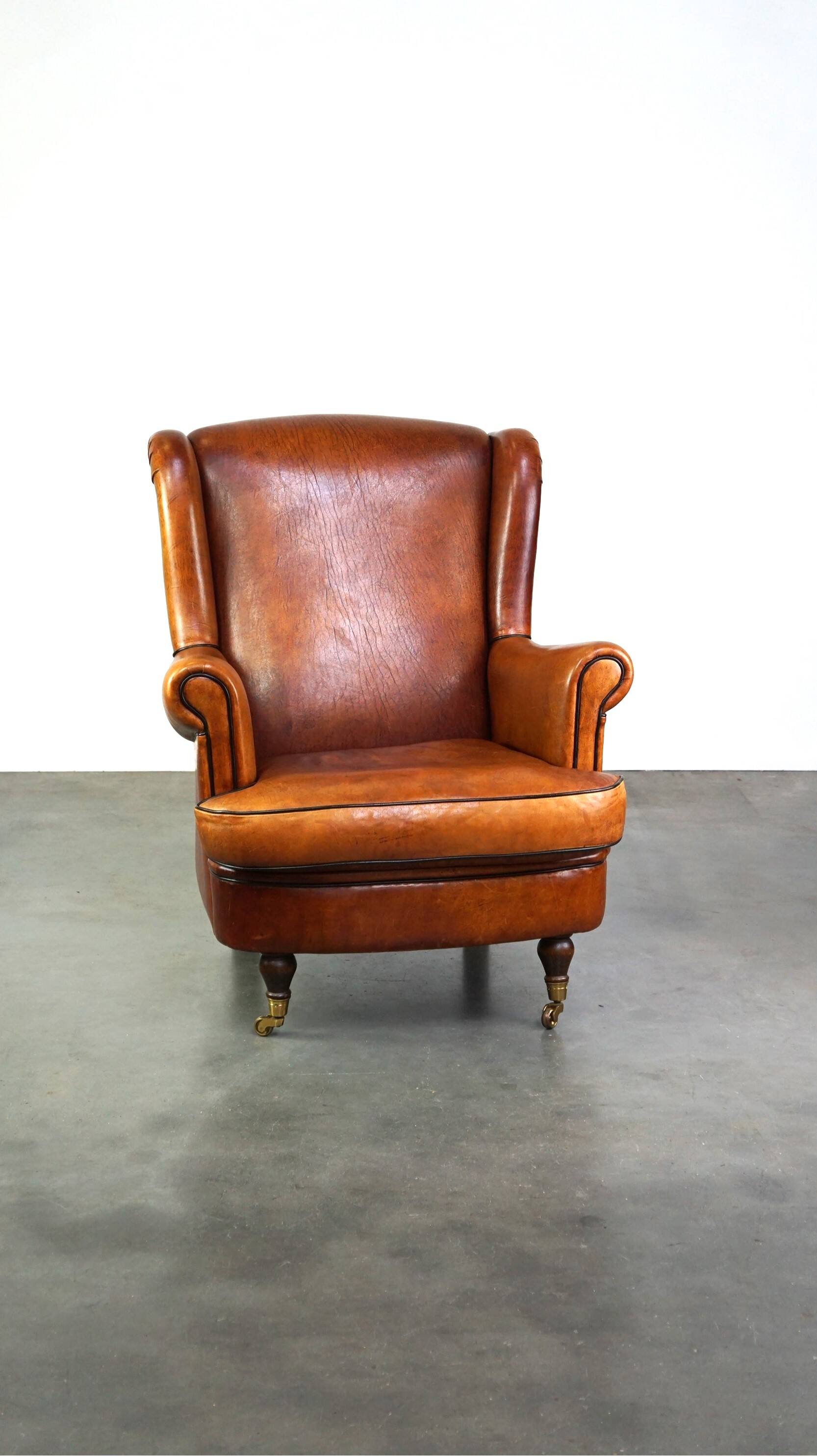 Subtle sheepskin wing chair in good condition on brass front wheels