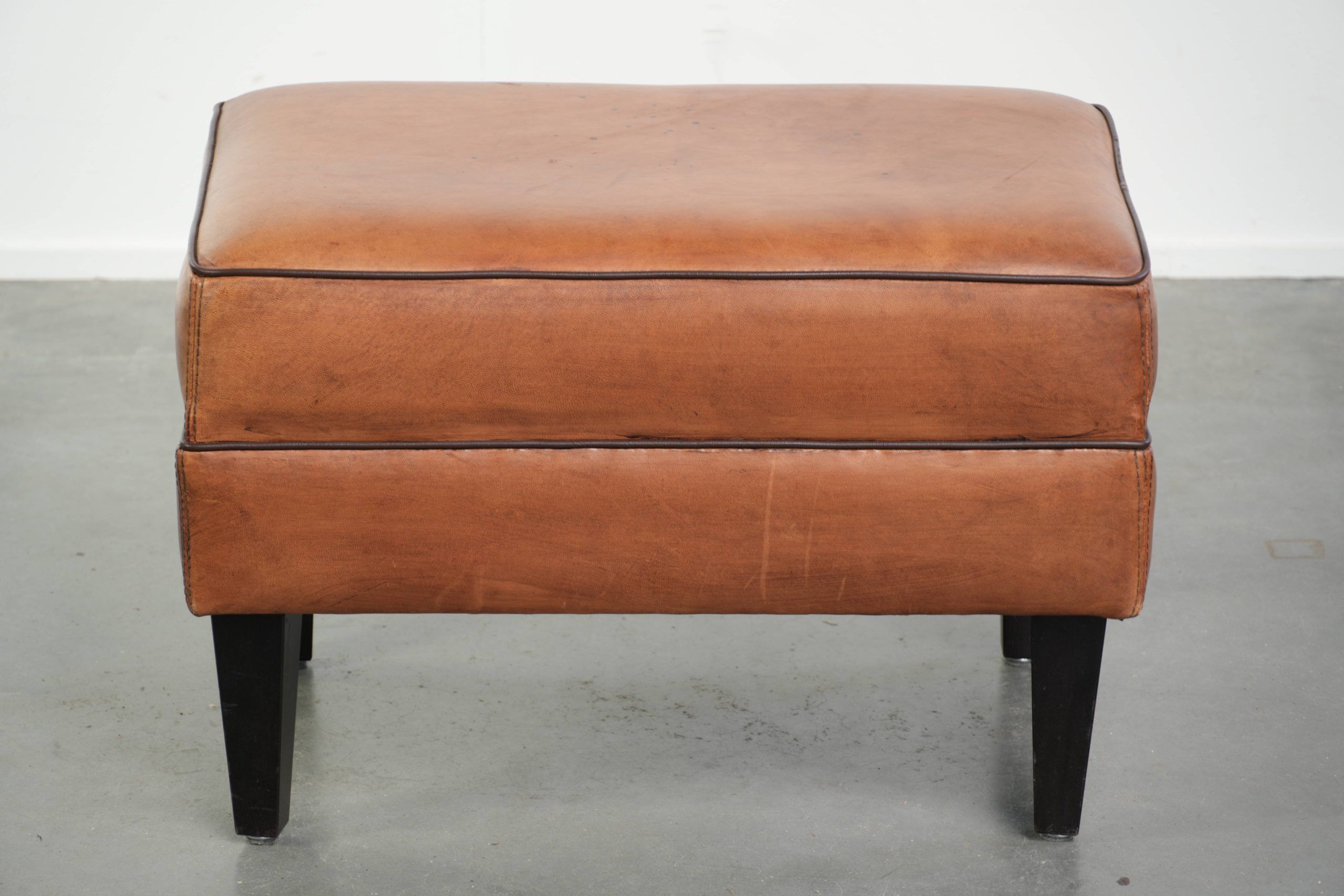 Handy sheepskin ottoman with warm colours finished with black piping