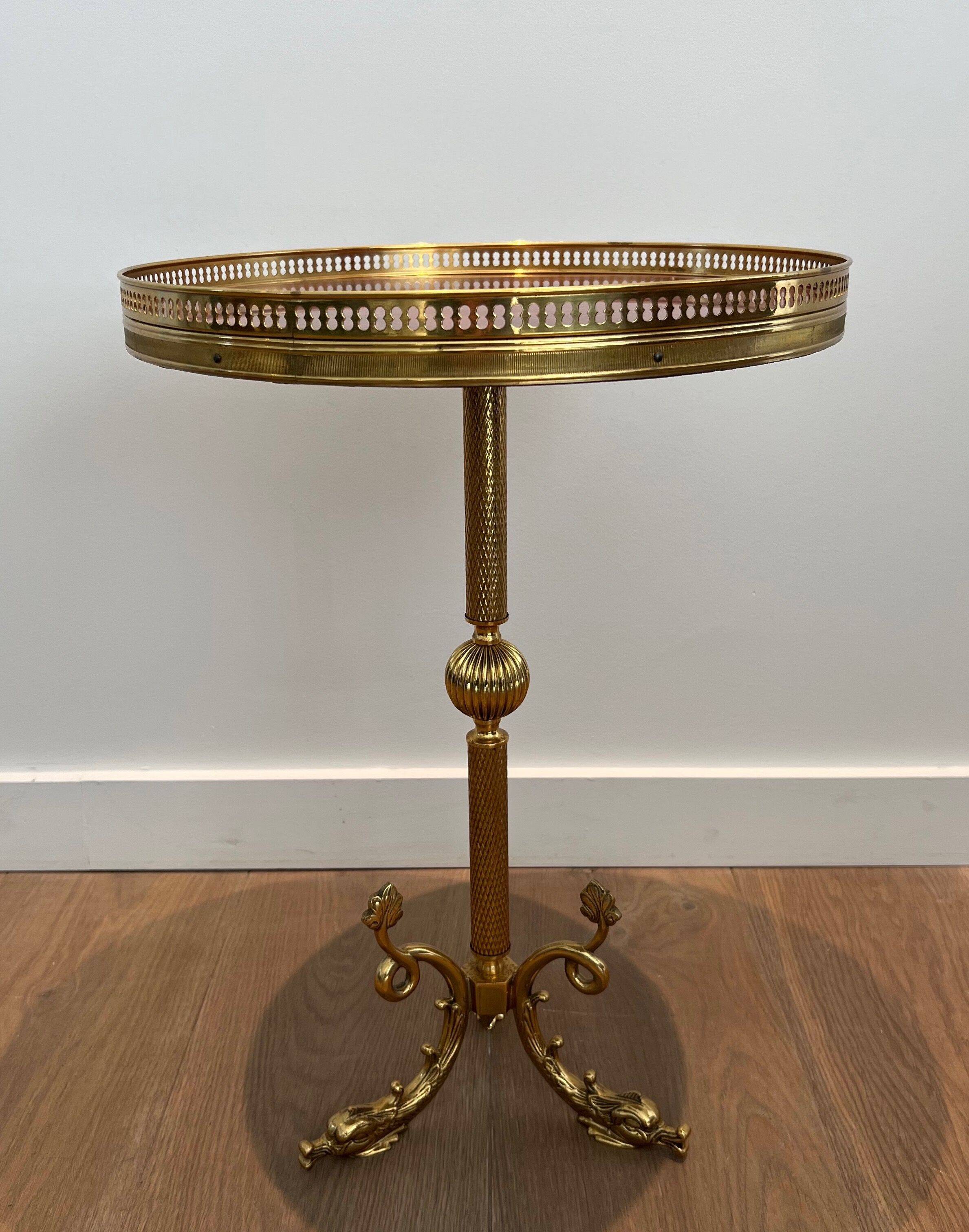 A round, neoclassical-style brass side table with a base decorated with dolphins and a red celluloid top encircled by an openwork gallery, attributed to the House of Jansen.