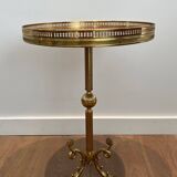 A round, neoclassical-style brass side table with a base decorated with dolphins and a red celluloid top encircled by an openwork gallery, attributed to the House of Jansen.