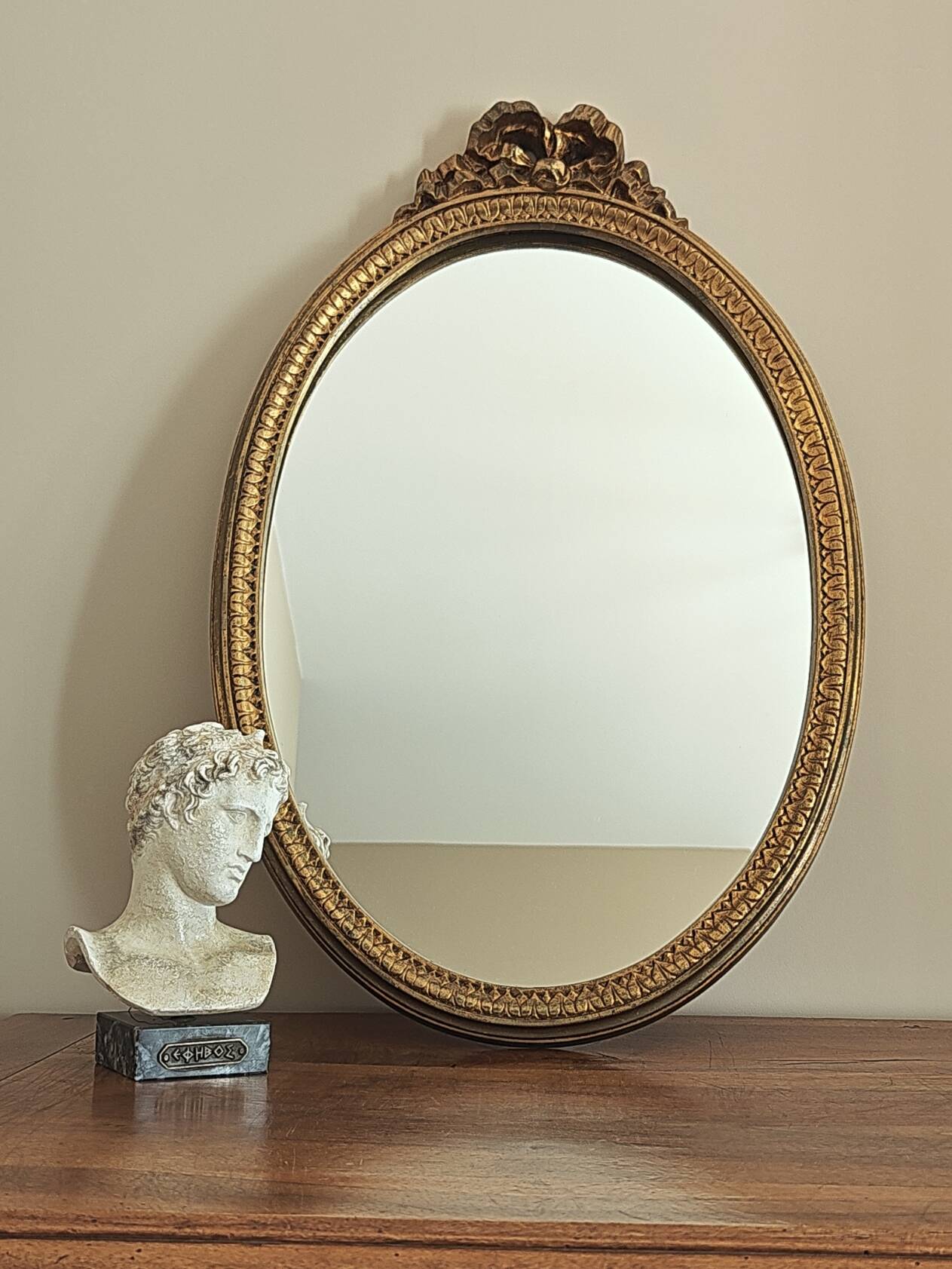 Vintage oval mirror with a carved wooden frame in gold, decorated with a bow.