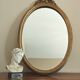 Vintage oval mirror with a carved wooden frame in gold, decorated with a bow.