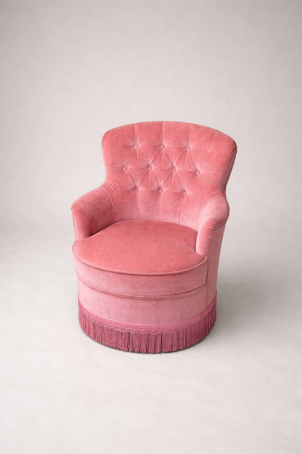 Vintage pink velvet tufted armchair with fringes.